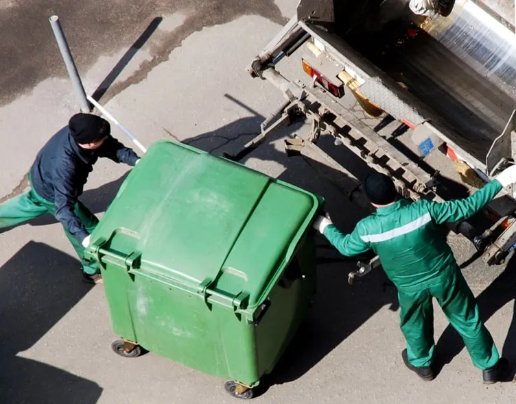 Hombre subiendo a un camión transportador toda la recolección de residuos industriales de un contenedor verde para procesarlo en Ecología empresarial.