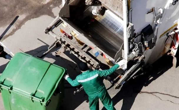 Hombre subiendo a un camión transportador toda la recolección de residuos industriales de un contenedor verde para procesarlo.